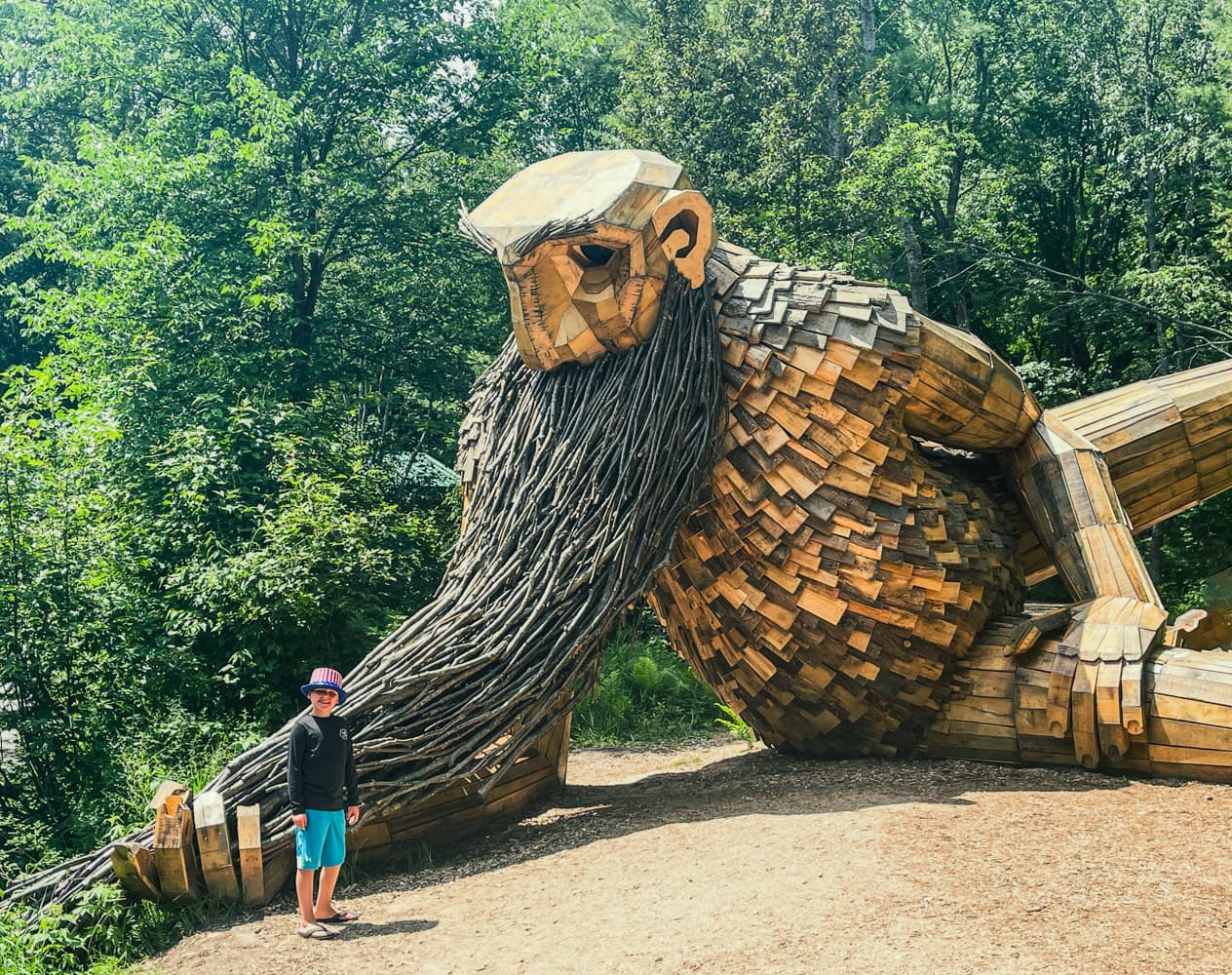 A young boy standing next to Benny the Beard Fisher's massive wooden beard for scale