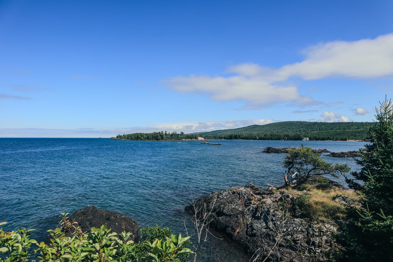 Blue Lake Superior water, rocky shoreline and forested hills near Eagle Harbor Lighthouse on a summer day