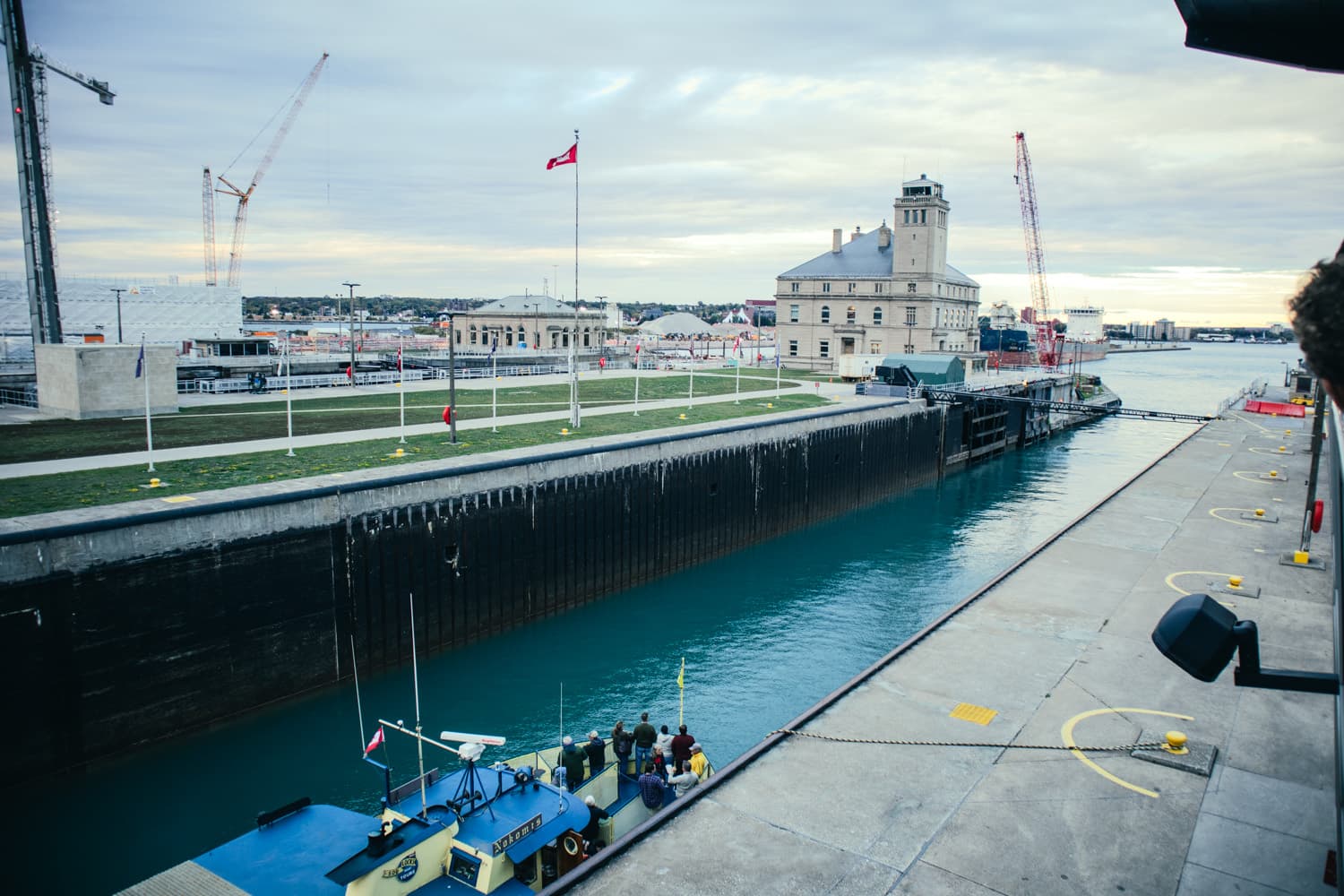 A tour boat inside one of the Soo Locks in Sault Ste. Marie, with construction cranes and the historic administration building beyond
