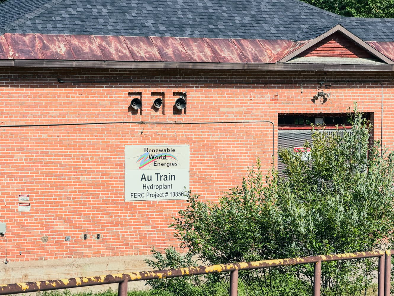Brick Au Train Hydroplant building with a Renewable World Energies sign reading Au Train Hydroplant, FERC Project #10856