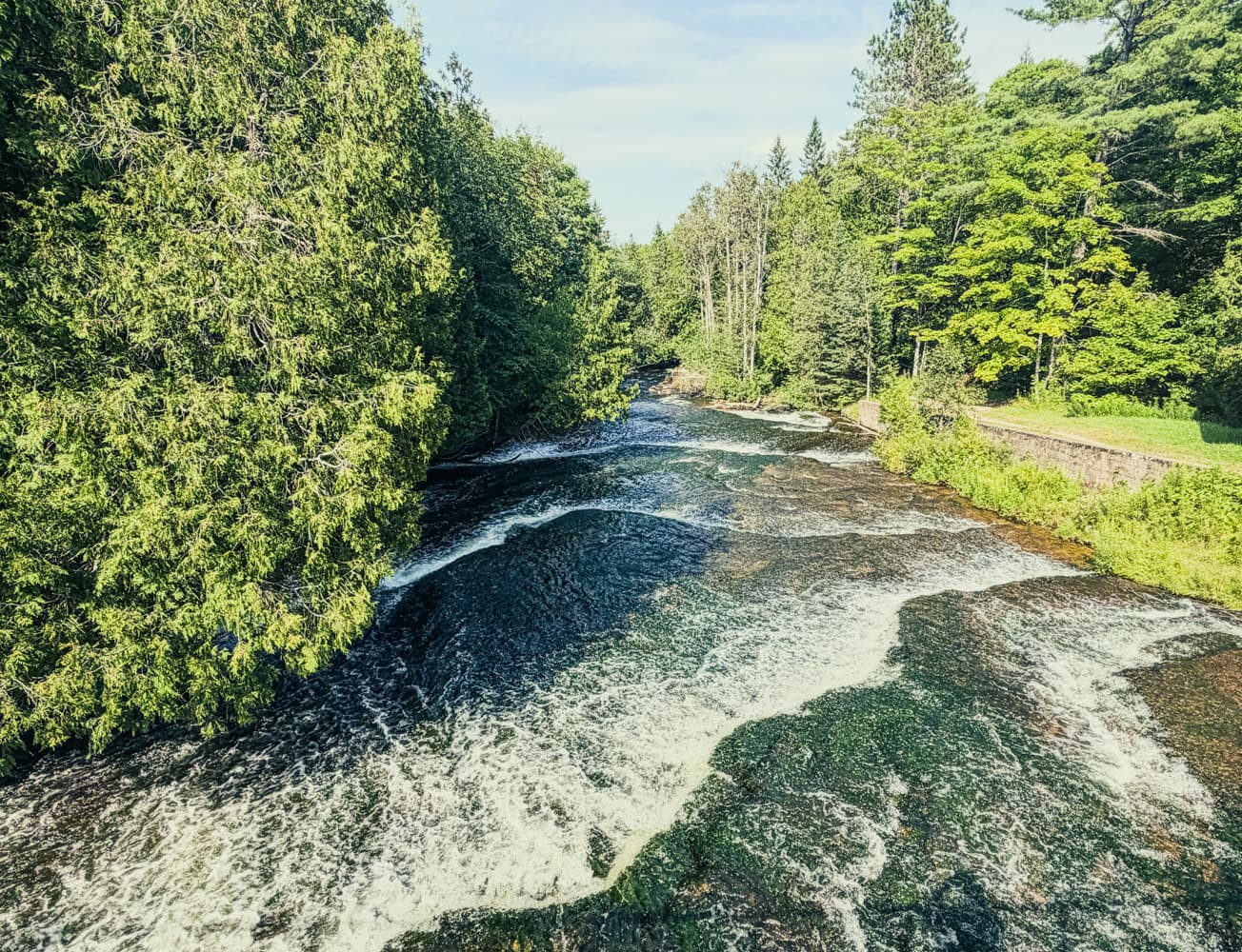 The Au Train River flowing past a concrete spillway structure and large pipes carrying water toward the hydroelectric plant