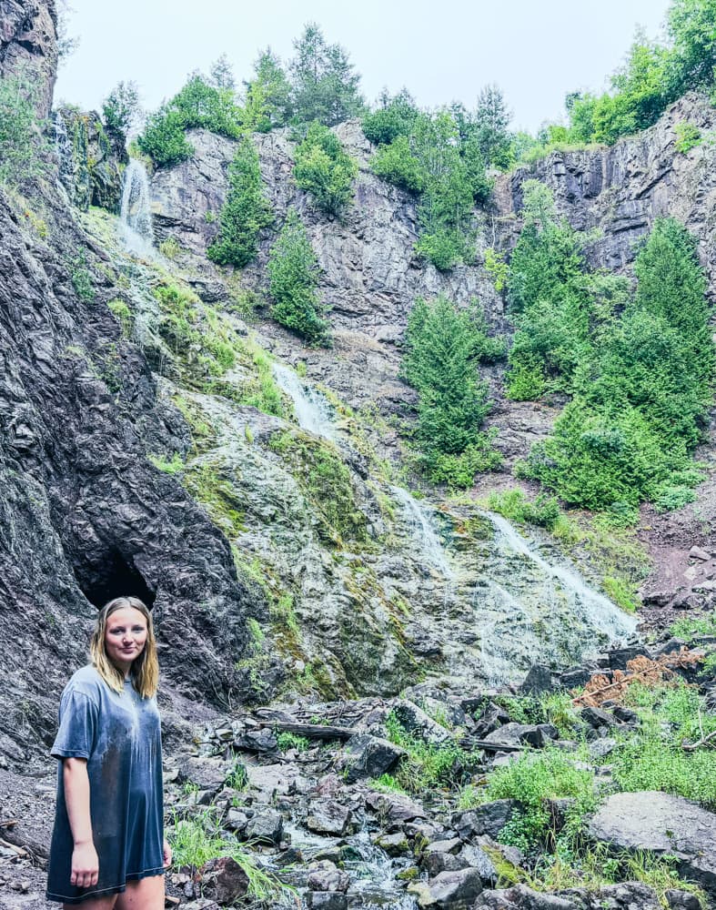 A visitor standing near a small cave at the base of the gorge close to Houghton Douglass Falls