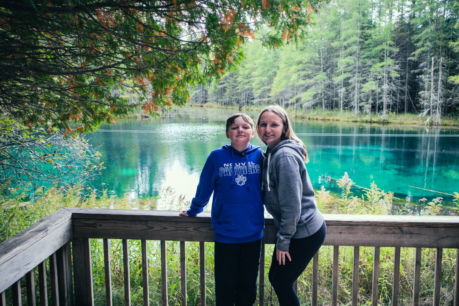 A brother and sister posing on the viewing deck above the turquoise water of Kitch-iti-kipi in the fall