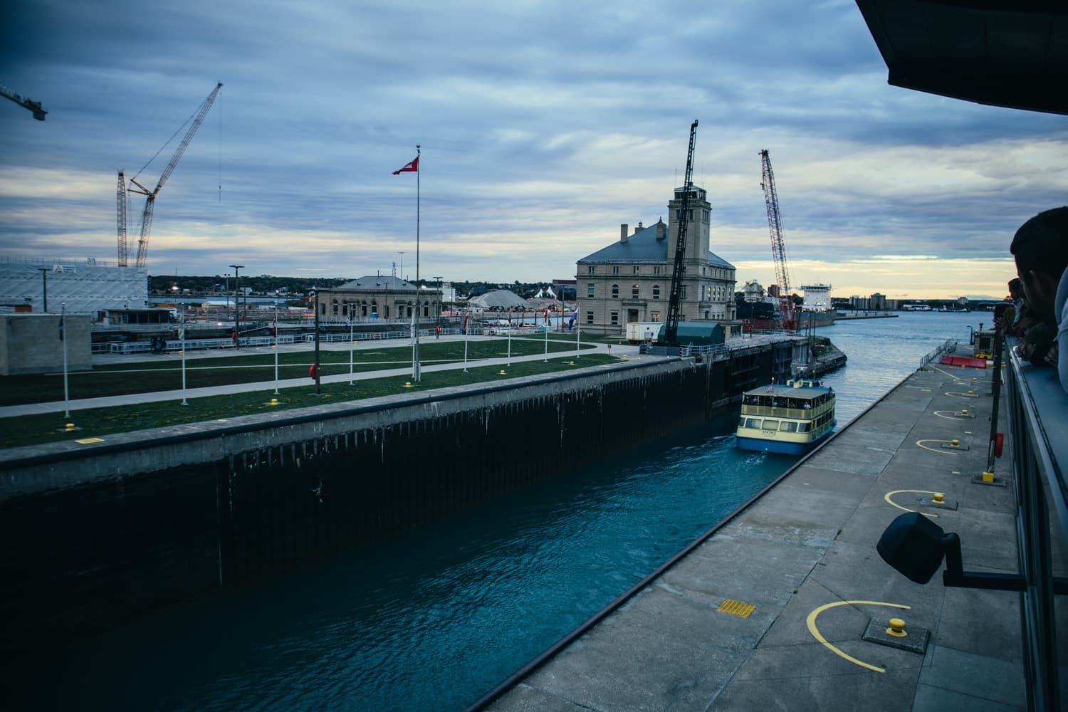 A boat waiting in a Soo Locks chamber at dusk as visitors watch from the observation platform