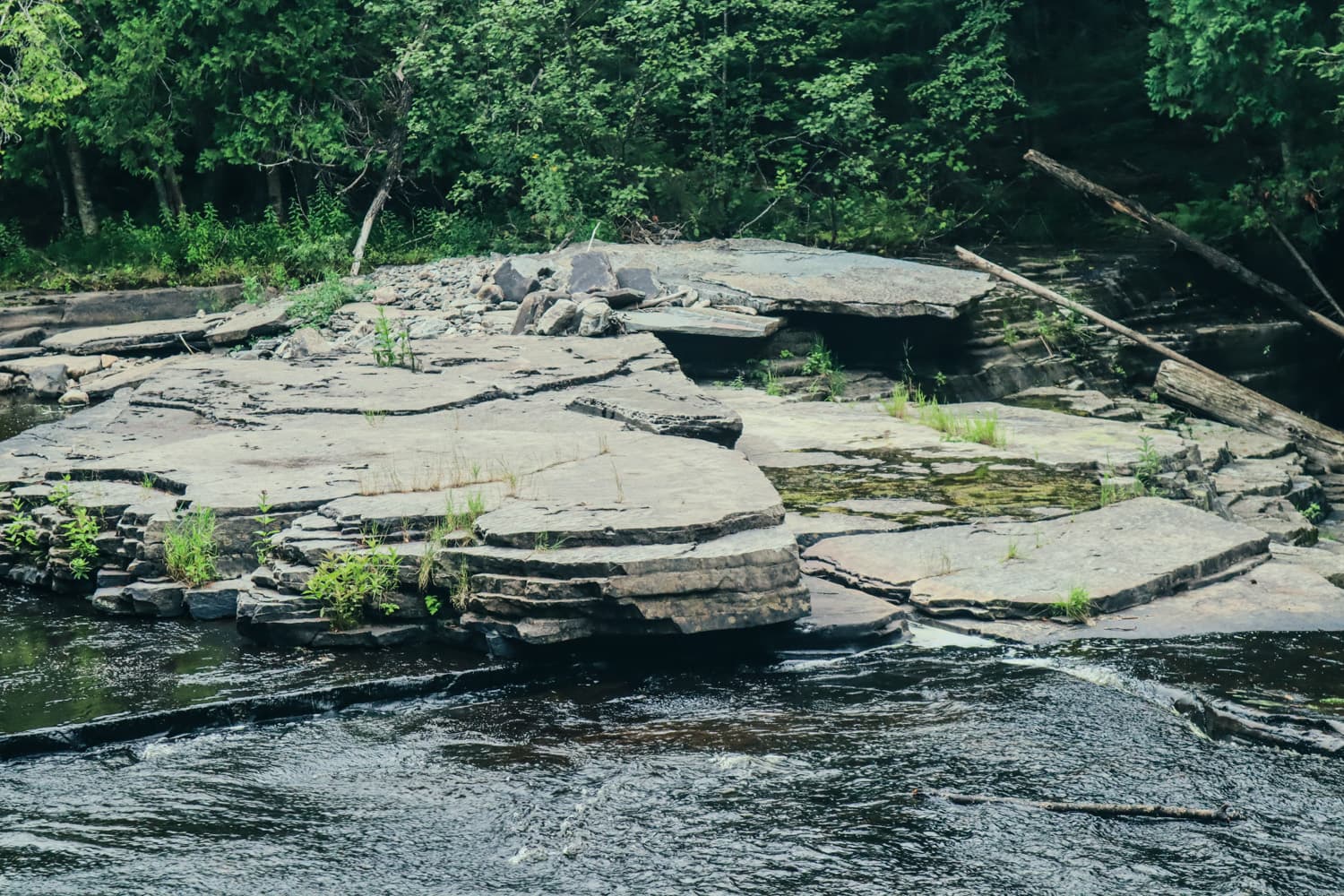 Layered flat rock shelves along the Sturgeon River at Canyon Falls, with forest behind