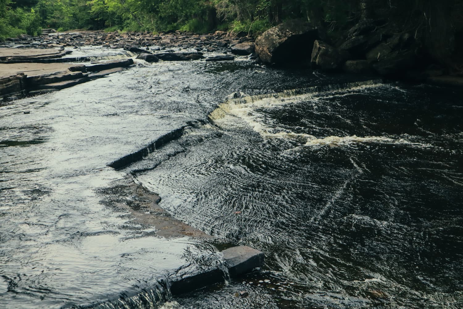 Water sliding over dark layered rock into a foaming pool at Canyon Falls on Michigan's Sturgeon River