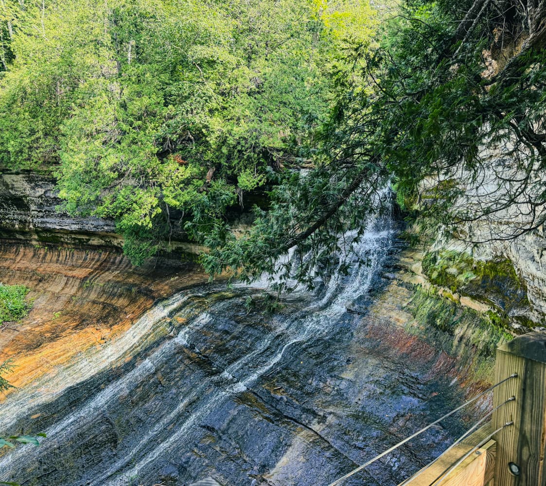 Close angled view of Laughing Whitefish Falls cascading over layered rock beneath overhanging evergreen branches
