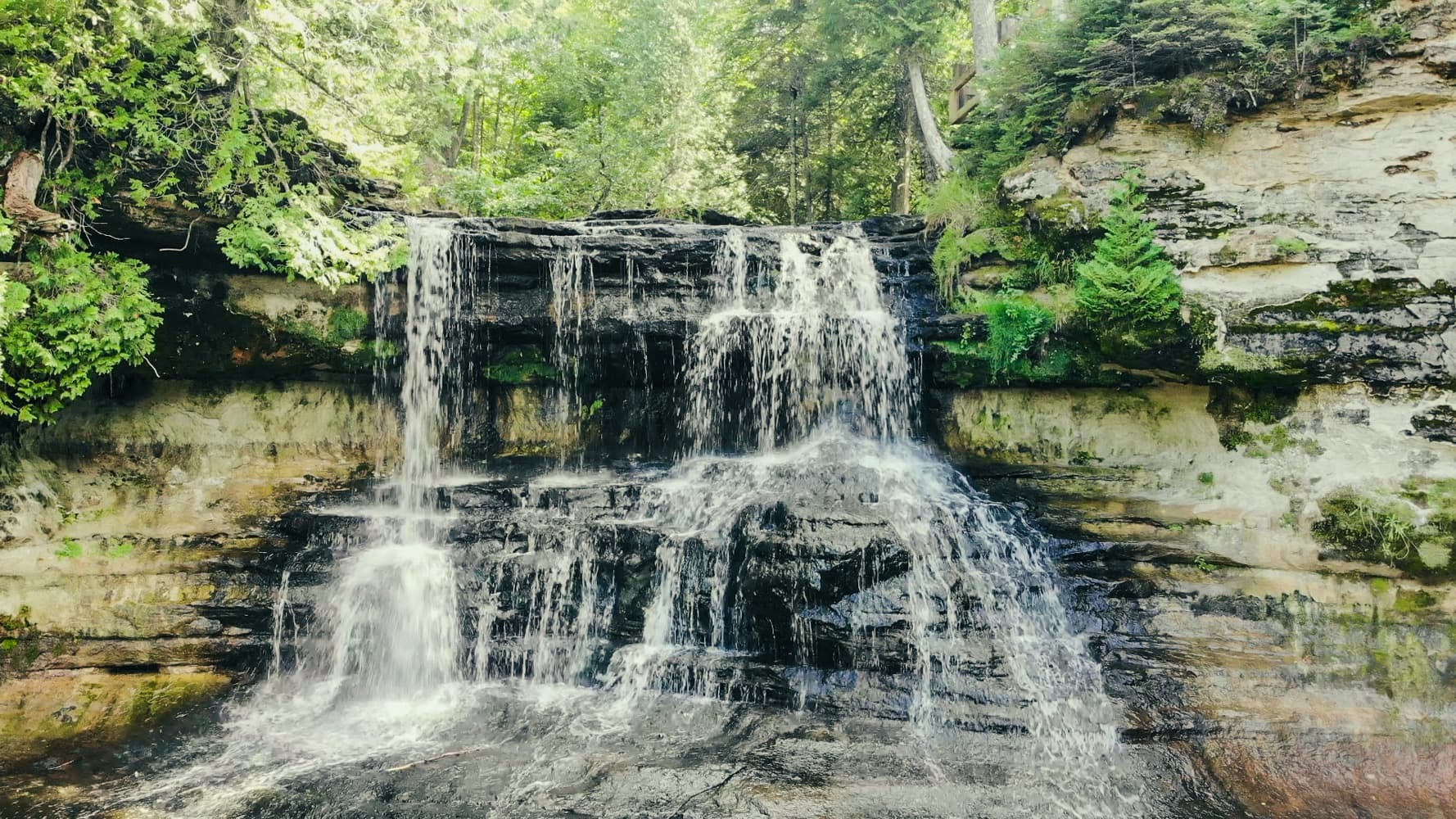 Laughing Whitefish Falls cascading down layered sandstone in a wooded Upper Peninsula gorge