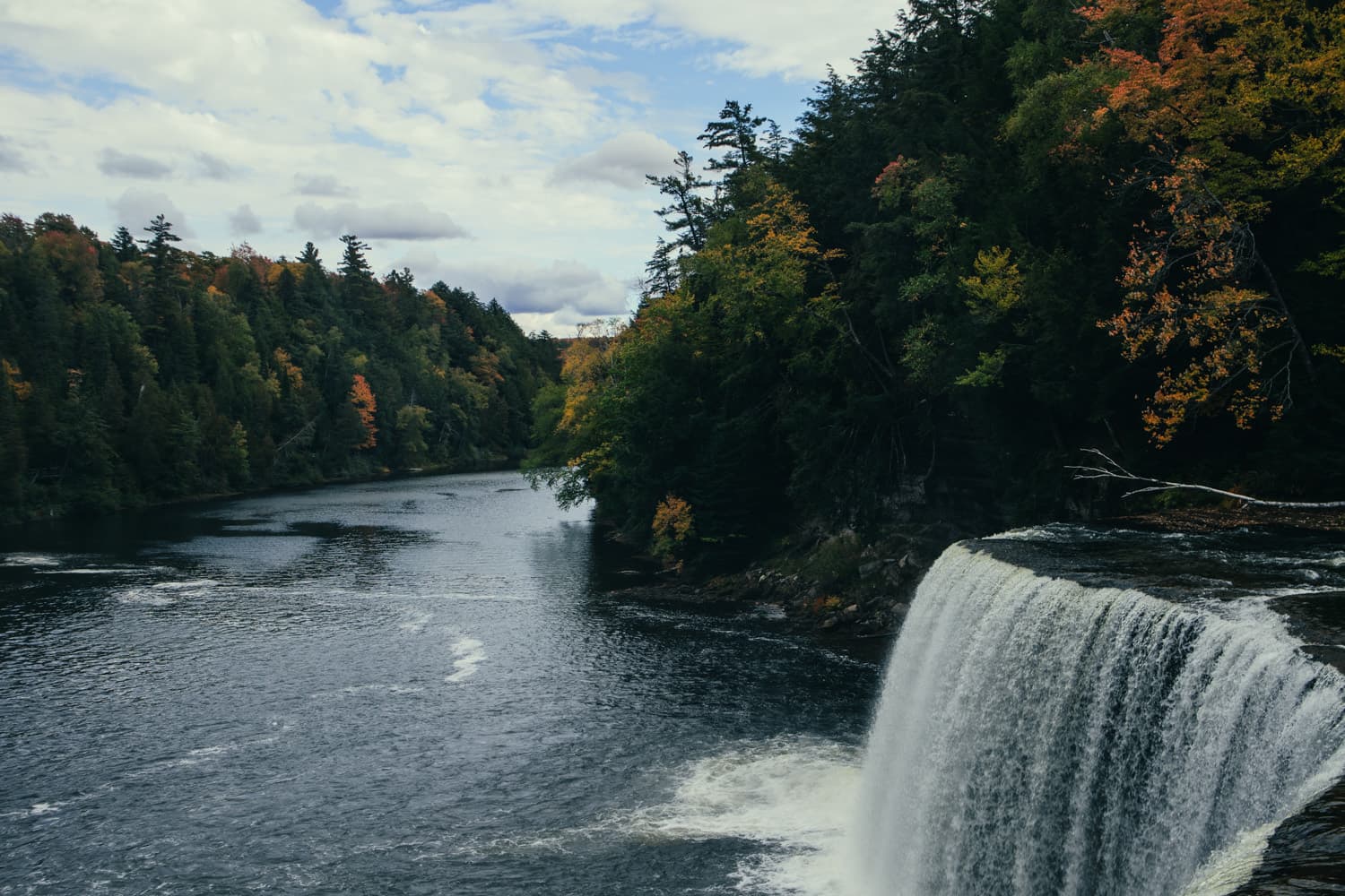 The Tahquamenon River flowing away from the edge of Upper Tahquamenon Falls between forested banks